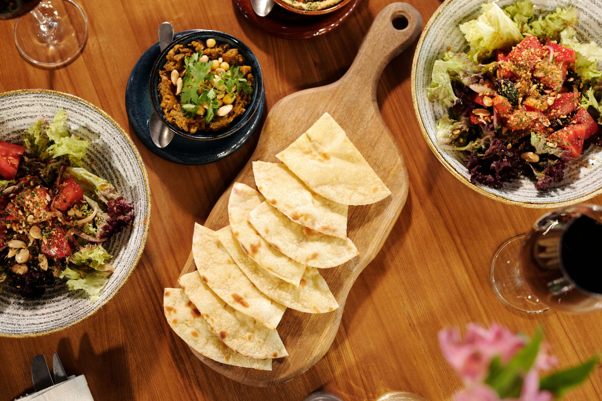 Ein farbenfrohes mediterranes Buffet mit Pita, Salaten und Wein auf einem Holztisch.