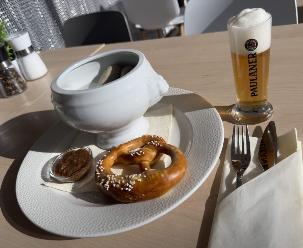 Teller mit Schüssel mit Weißwurst, Breze und Senf, daneben Paulaner-Glas mit Bier, Roots